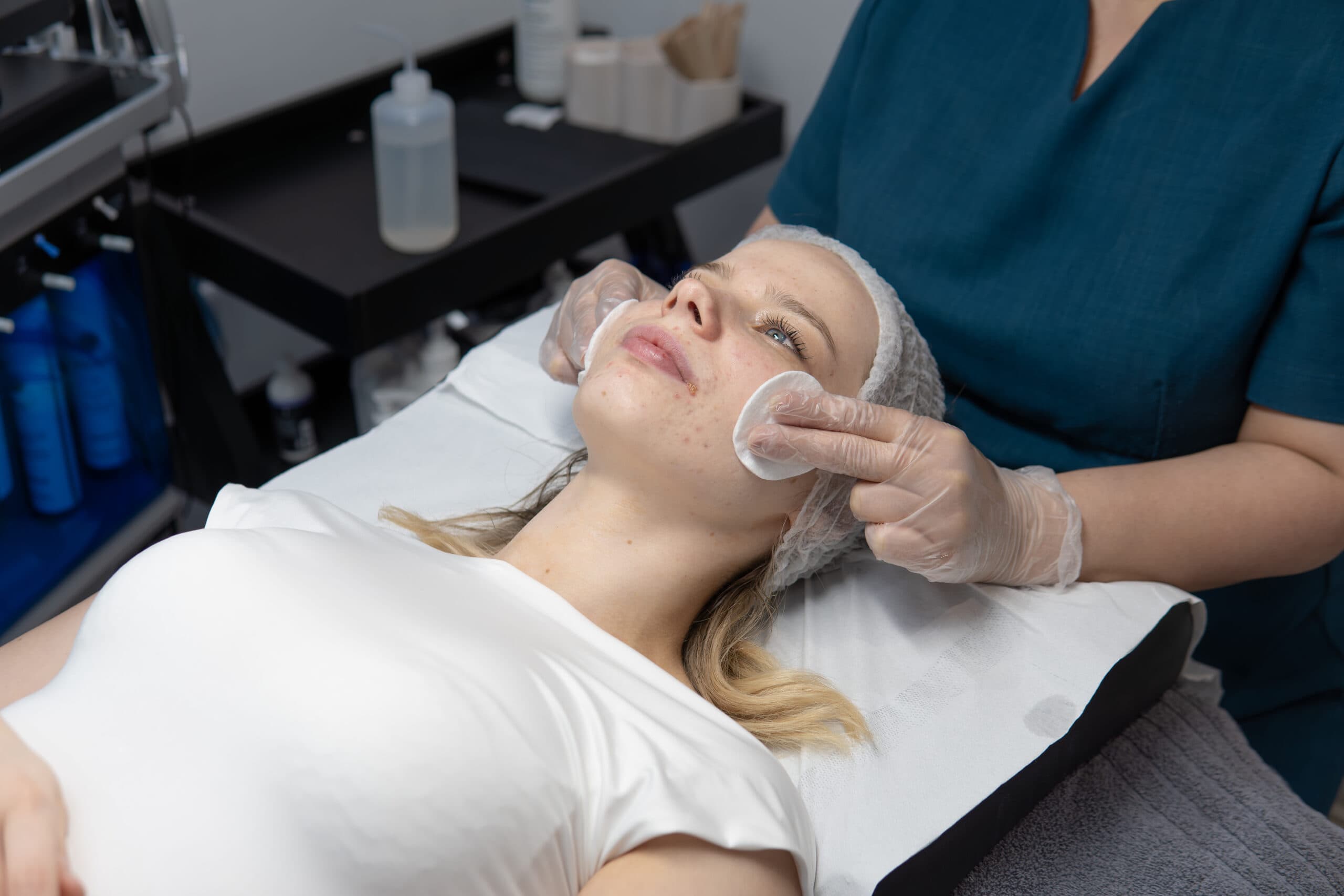 A woman receiving a facial chemical peel treatment from a skincare expert at an aesthetic clinic