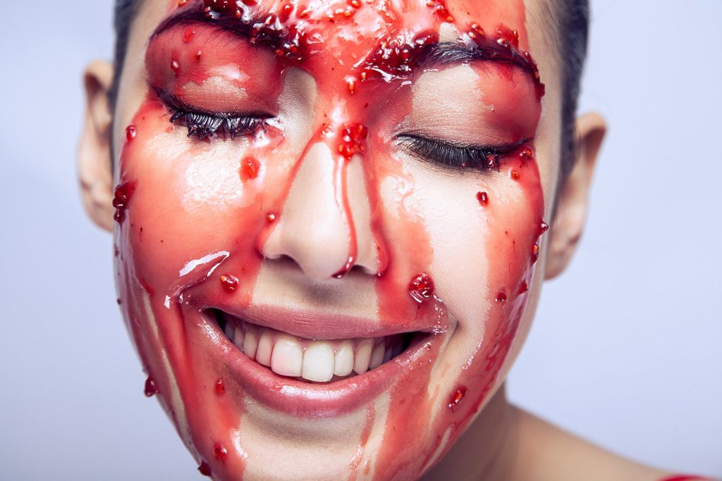 Woman smiling during a Vampire Facial treatment with red serum mask applied to face – PRP therapy skincare concept