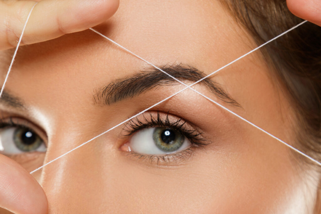 Close-up of a woman’s eyebrow threading procedure for precise brow shaping.